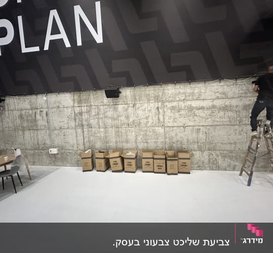 אדם על סולם מתקין שלט גדול על קיר בטון